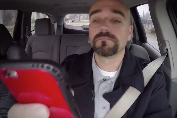 a man driving and looking at his red cell phone