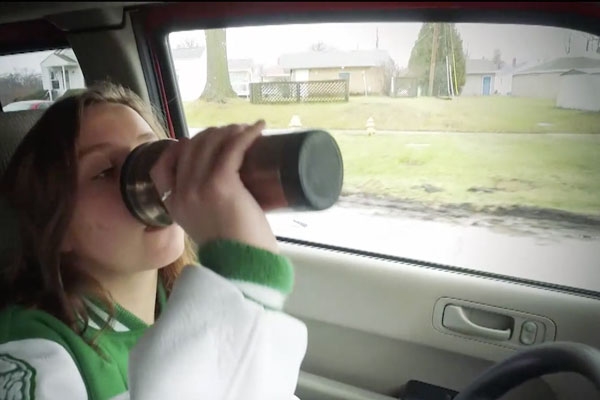 a teen girl driving while drinking out of an insulated travel cup