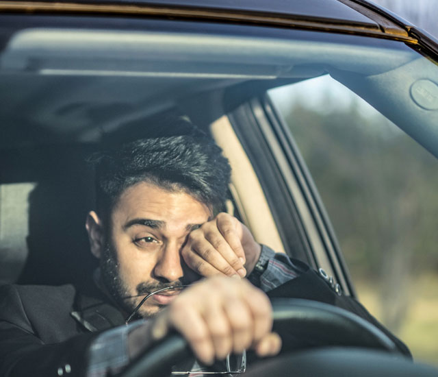 a man driving rubbing his eyes