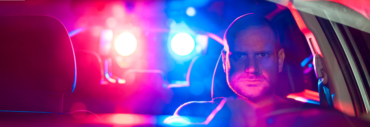 an angry man behind the wheel with police lights shining through the car