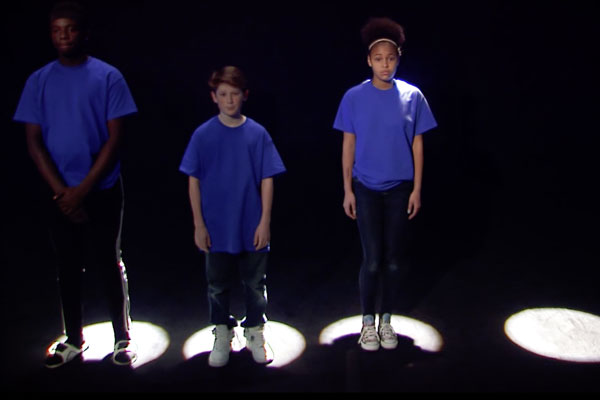 three teens standing in lighted spots on the floor in a black room