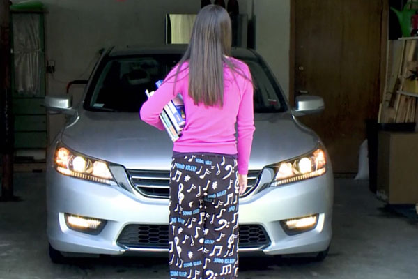 a teen girl in a pink shirt and sleep pajamas standing in front of a car