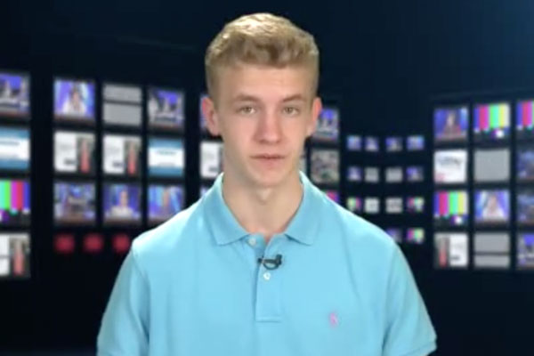 a teen anchor in a blue shirt with a monitor background