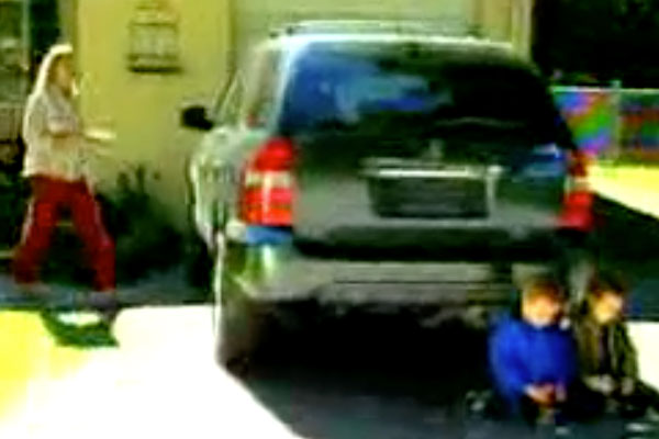 a woman walking to her car with two kids playing by the back wheel