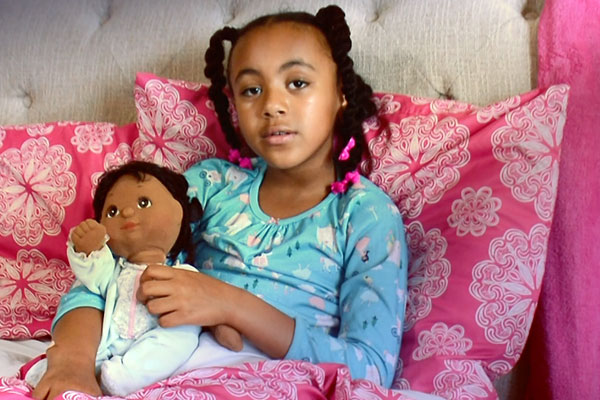 a young girl sitting with pink cushions holding a doll 